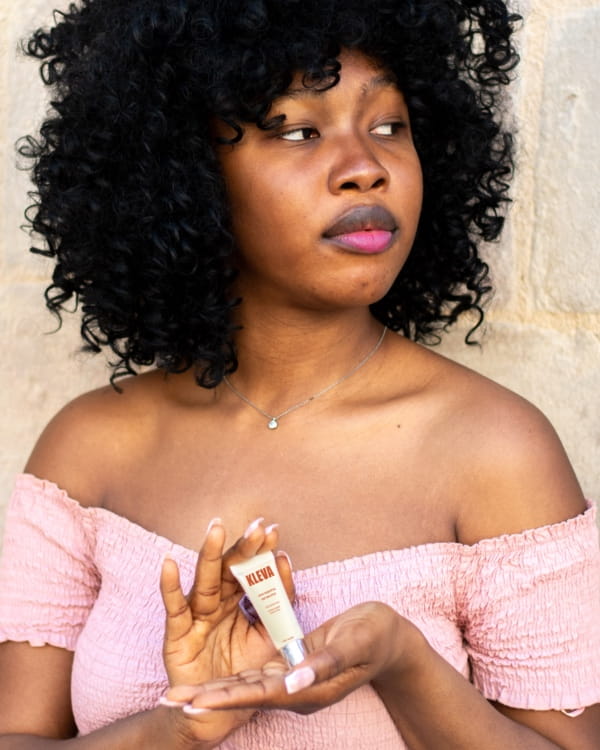 Jeune femme tenant la colle corporelle KLEVA, vêtue d’un top rose épaules dénudées, mettant en avant une tenue impeccable et sécurisée.