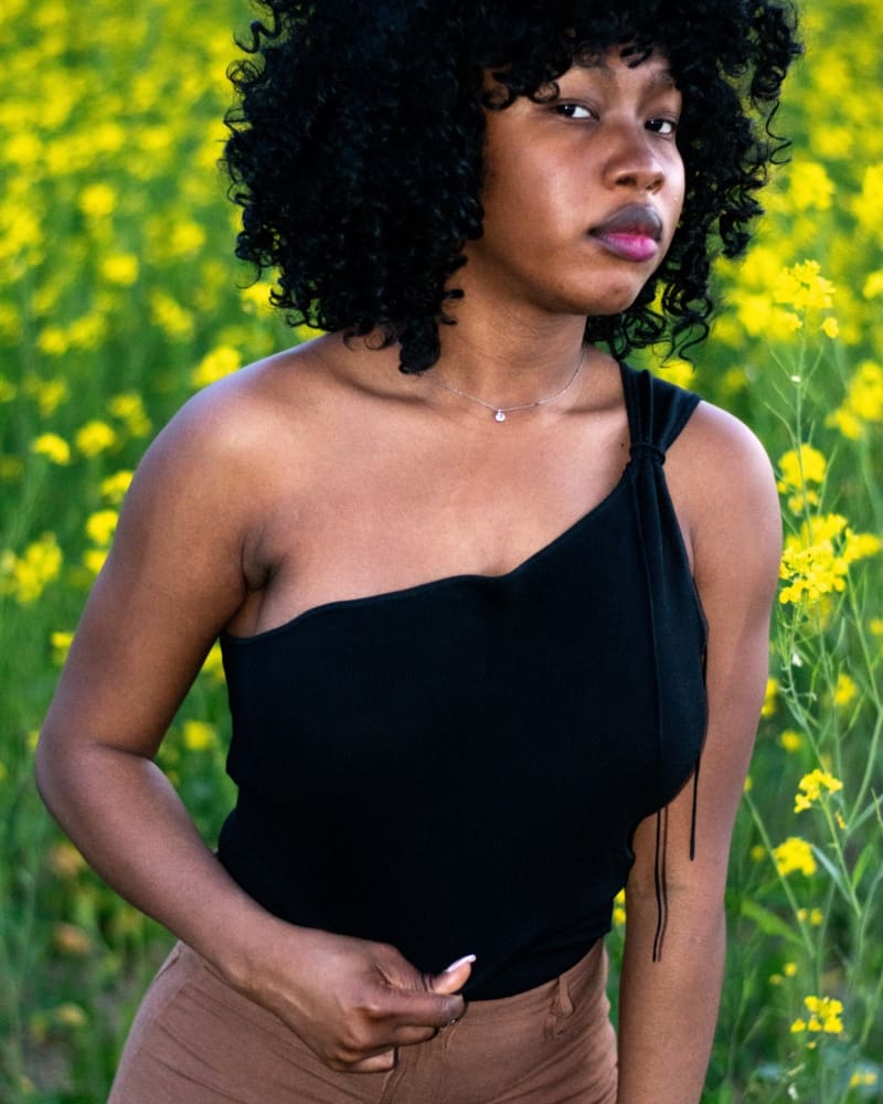 Femme portant un top asymétrique noir maintenu en place grâce à la colle corporelle KLEVA, démontrant la tenue parfaite du vêtement même en tirant dessus.